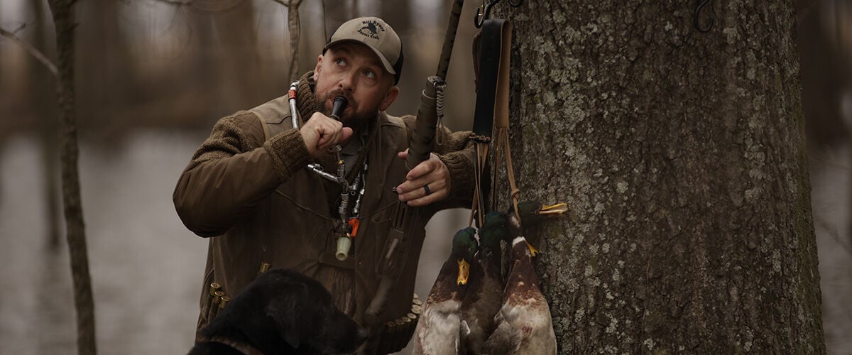Man leaning against tree with duck call